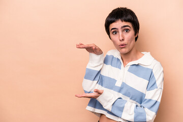 Young caucasian woman isolated on beige background shocked and amazed holding a copy space between hands.