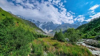 Fototapeta na wymiar Patara Enguri River flowing down the a valley with view on the Shkhara Glacier in the Greater Caucasus Mountain Range in Georgia, Svaneti Region,Ushguli. Snow-capped mountains, Blooming flowers.