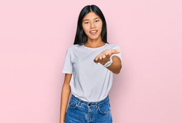Beautiful young asian woman wearing casual white t shirt smiling cheerful offering palm hand giving assistance and acceptance.