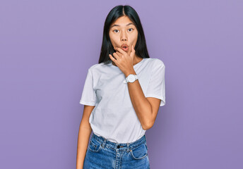 Beautiful young asian woman wearing casual white t shirt looking fascinated with disbelief, surprise and amazed expression with hands on chin