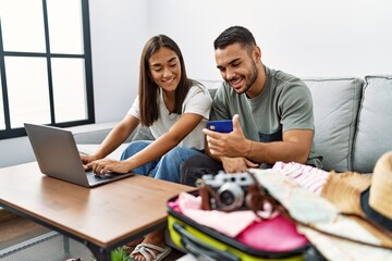 Latin man and woman couple smiling confident paying for travel using laptop and credit card at home