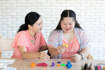 down syndrome girl with woman teacher learning about sculpt plasticine figures on a table