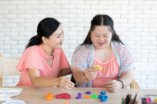 Down Syndrome Girl With Woman Teacher Learning About Sculpt Plasticine Figures On A Table