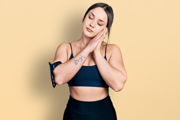 Obraz premium Young hispanic woman wearing sportswear sleeping tired dreaming and posing with hands together while smiling with closed eyes.