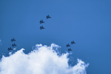 Group of military aircraft shows aerobatics in blue sky against background of clouds. Parade of army air force over the city. Performance of victory.