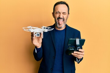 Middle age hispanic man using drone sticking tongue out happy with funny expression.