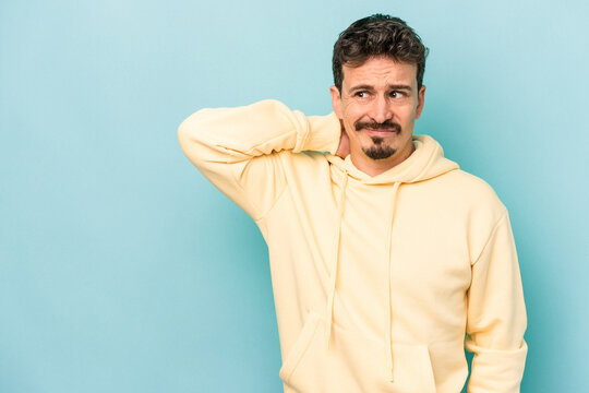 Young caucasian man isolated on blue background touching back of head, thinking and making a choice.