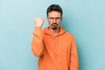 Young caucasian man isolated on blue background showing fist to camera, aggressive facial...