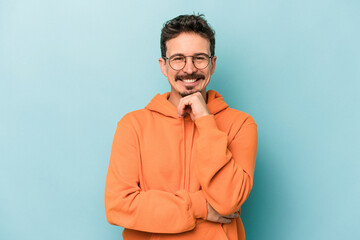 Fototapeta premium Young caucasian man isolated on blue background smiling happy and confident, touching chin with hand.