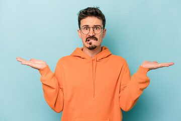 Fototapeta premium Young caucasian man isolated on blue background confused and doubtful shrugging shoulders to hold a copy space.