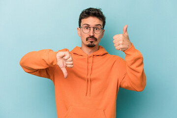 Young caucasian man isolated on blue background showing thumbs up and thumbs down, difficult choose...