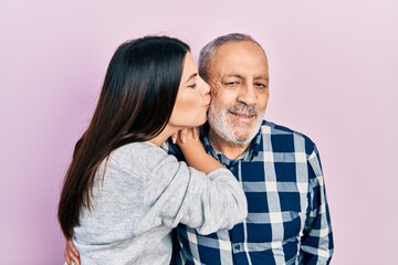 Young brunette woman and senior man standing over pink background. Daughter and father hugging and...