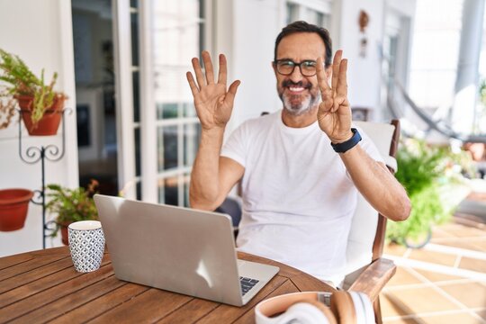 Middle age man using computer laptop at home showing and pointing up with fingers number eight while smiling confident and happy.