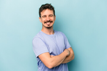 Young caucasian man isolated on blue background who feels confident, crossing arms with determination.