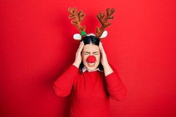 Young hispanic woman wearing deer christmas hat and red nose suffering from headache desperate and stressed because pain and migraine. hands on head.