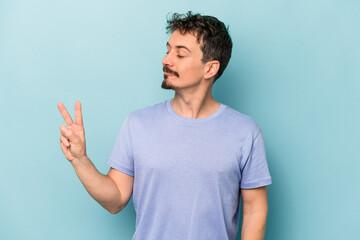 Fototapeta premium Young caucasian man isolated on blue background joyful and carefree showing a peace symbol with fingers.