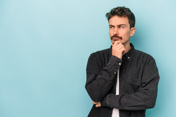 Young caucasian man isolated on blue background looking sideways with doubtful and skeptical expression.