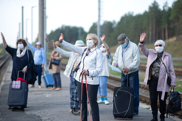 A group of senior friends in face masks on the platform waiting for a train