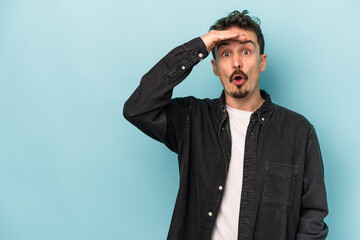 Fototapeta premium Young caucasian man isolated on blue background looking far away keeping hand on forehead.