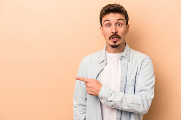 Young caucasian man isolated on beige background pointing to the side