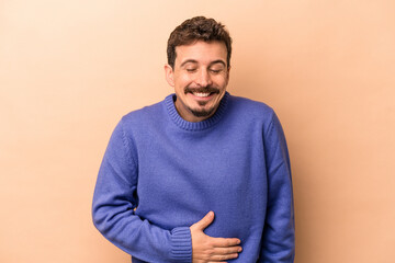 Young caucasian man isolated on beige background touches tummy, smiles gently, eating and satisfaction concept.