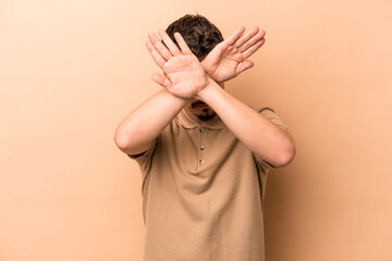 Young caucasian man isolated on beige background keeping two arms crossed, denial concept.