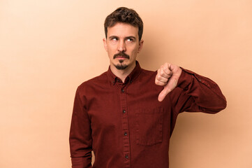 Obraz premium Young caucasian man isolated on beige background showing a dislike gesture, thumbs down. Disagreement concept.