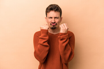 Young caucasian man isolated on beige background showing fist to camera, aggressive facial...