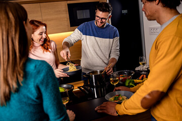 Group of friends having dinner party at home drinking wine and preparing vegetarian food.