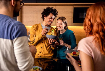 Group of friends having dinner party at home drinking wine and preparing vegetarian food.