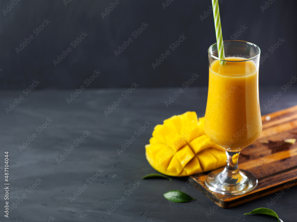 Wall mural yellow exotic smoothie with mango in a glass with a straw. dark background and copy space