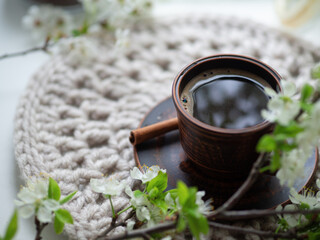 Obraz na płótnie Canvas A cup of espresso coffee on a knitted stand and a blooming branch of a white cherry. Spring morning