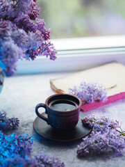 Obraz na płótnie Canvas Spring still life with a cup of coffee and bouquets of lilacs. Colored light. Reading a book and drinking coffee by the window, spring mood