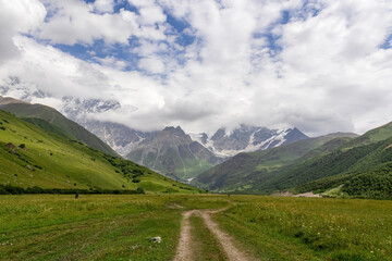 Fototapeta na wymiar A hiking path leading to the Shkhara Glacier in the Greater Caucasus Mountain Range in Georgia, Svaneti Region, Ushguli. Snow-capped mountains in the back. Wanderlust. Wilderness. Overcast and clouds