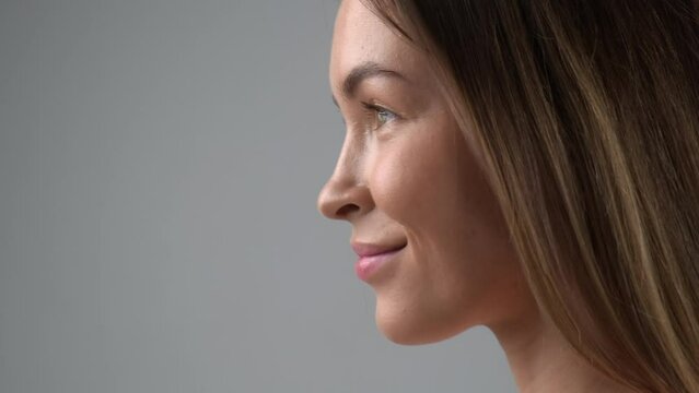 Beauty face of a young blonde woman in profile close-up. Smile, beautiful eyes, lips and teeth. Grey background