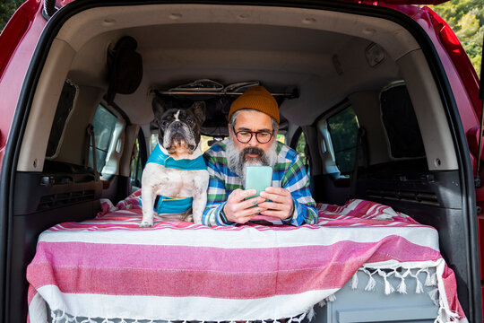 Elderly man browsing phone in camper with dog