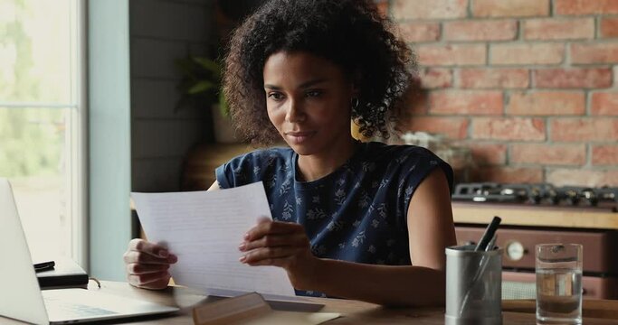 Young African woman getting mail take paper document out of envelop feel excited with job offer being hired accepted to college university. Amazed millennial lady read great news in official letter