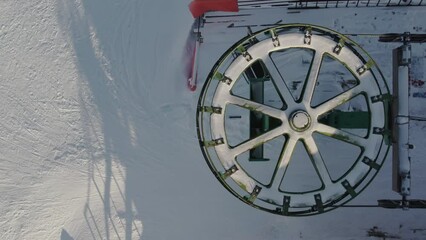 Top view of a large wheel chairlift for transporting skiers and snowboarders on a snow-covered slope. A ski lift cable car for transporting people on a winter mountain in a ski resort. 4k ProRes 422 - Powered by Adobe
