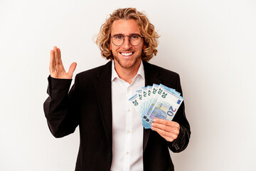 Young caucasian business man holding banknotes isolated on white background receiving a pleasant...