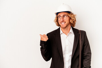 Young architect caucasian man with helmet isolated on white background points with thumb finger away, laughing and carefree.