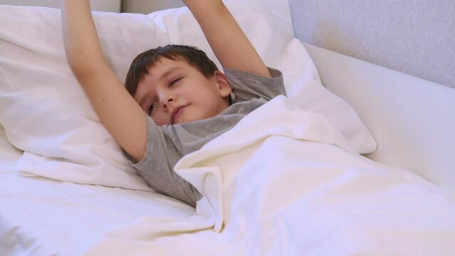 a seven-year-old boy wakes up and stretches out lying on the bed