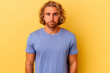 Young caucasian man isolated on yellow background blows cheeks, has tired expression. Facial expression concept.