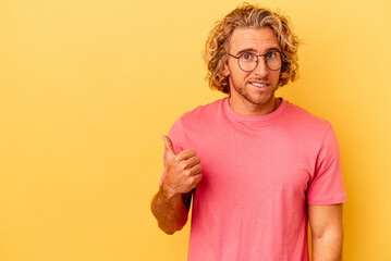 Young caucasian man isolated on yellow background shocked pointing with index fingers to a copy space.