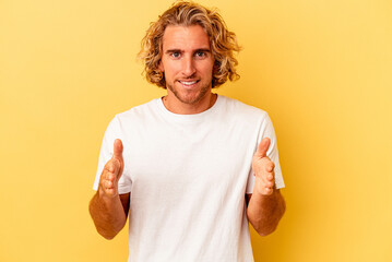 Young caucasian man isolated on yellow background holding something with both hands, product presentation.