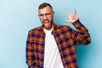 Naklejka premium Young caucasian man isolated on blue background showing a horns gesture as a revolution concept.