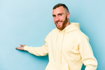 Young caucasian man isolated on blue background showing a welcome expression.