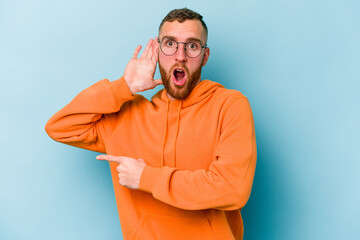 Young caucasian man isolated on blue background trying to listening a gossip.