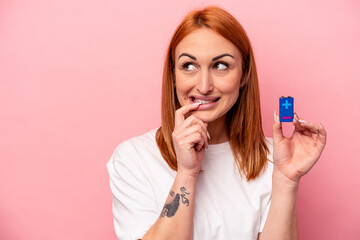 Young caucasian woman holding a batteries isolated on pink background relaxed thinking about something looking at a copy space.