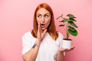 Young caucasian woman holding a plant isolated on pink background Young caucasian woman holding a...