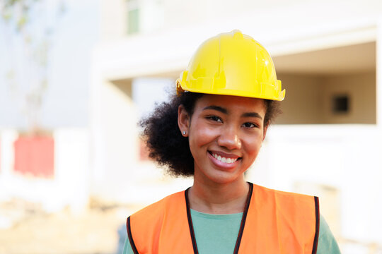 Close Up Face Black Woman. Portrait Femal African American Engineer Worker Wearing Yellow Hard Hat Helmet Working On Construction Site.